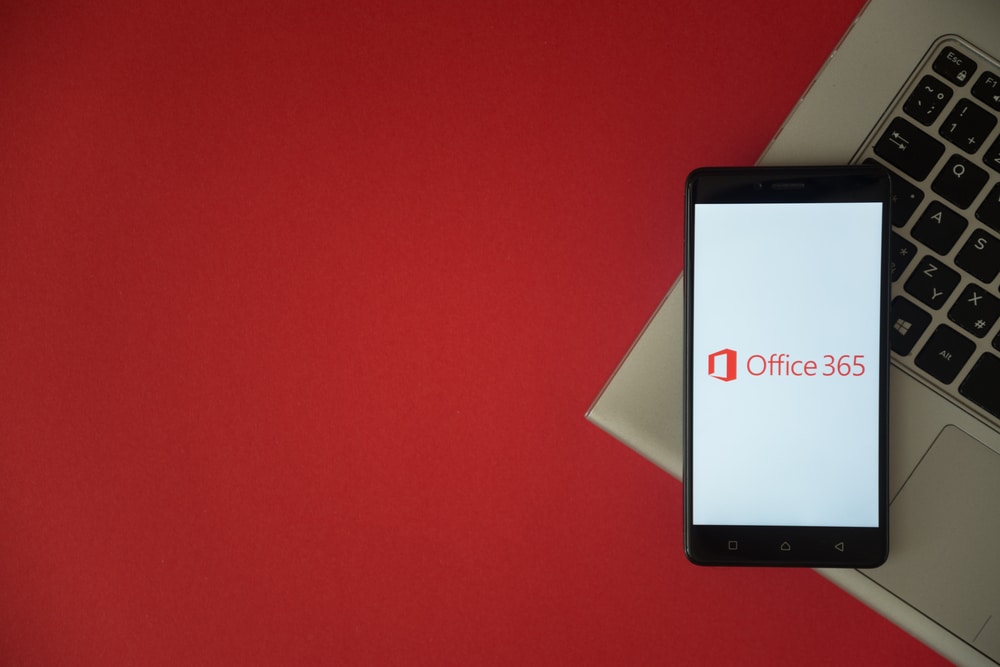 London, United Kingdom, October 23, 2017 Microsoft office 365 logo on smartphone screen placed on laptop keyboard. Empty place to write information with red background.