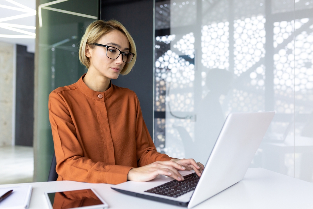 Serious and confident woman boss working at workplace inside office with laptop, business woman thinking typing on computer keyboard, blonde company worker programmer developer.