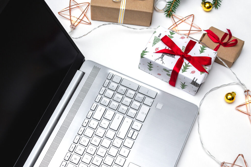 Laptop keyboard surrounded by holiday gifts, decorative lights, and festive ornaments, emphasizing online shopping during the holiday season and awareness of potential scams.
