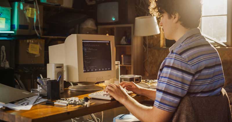 Computer Engineer Programming On Old Desktop Computer In Retro Garage. Experienced Software Developer Writing Code For New Innovative Portable Device Startup In Nostalgic Nineties.