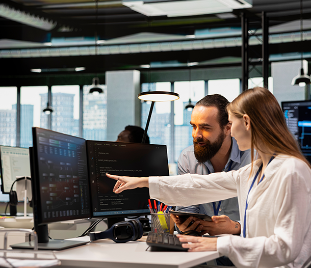 Two colleagues collaborating in a modern office, discussing data displayed on computer monitors, emphasizing teamwork and technology in a business environment.