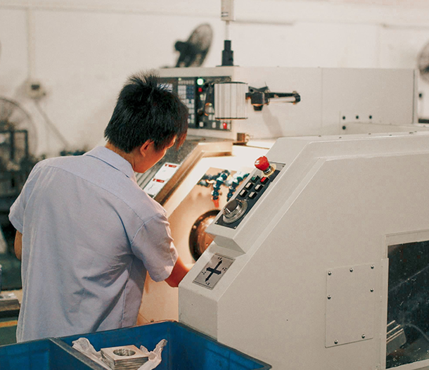 Factory worker in a light blue shirt operating a CNC milling machine, adjusting the control panel.