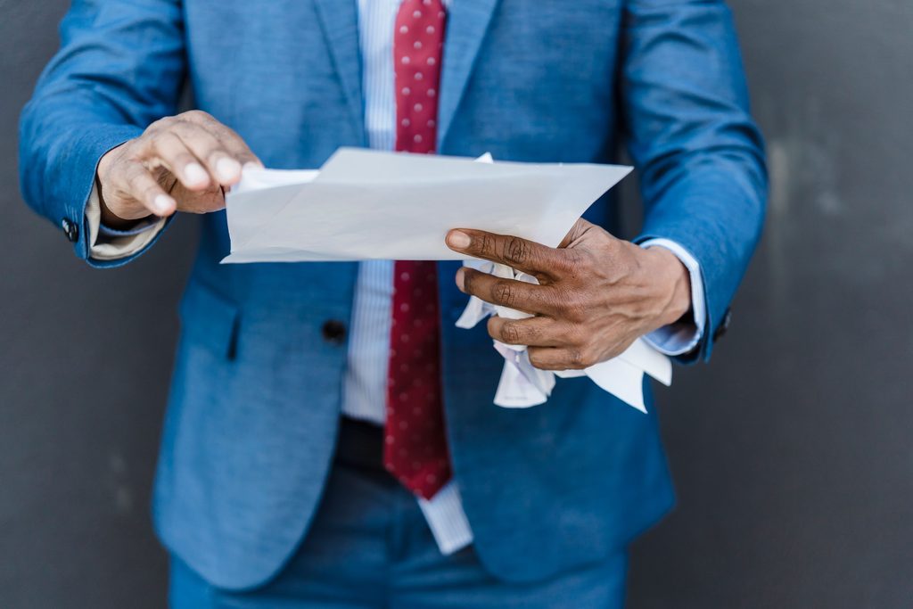 pexels-nicola-barts-7925821 | LG Networks, Inc. Business owner in a blue suit reading a letter while holding crumpled papers, reviewing a notice from a managed IT provider